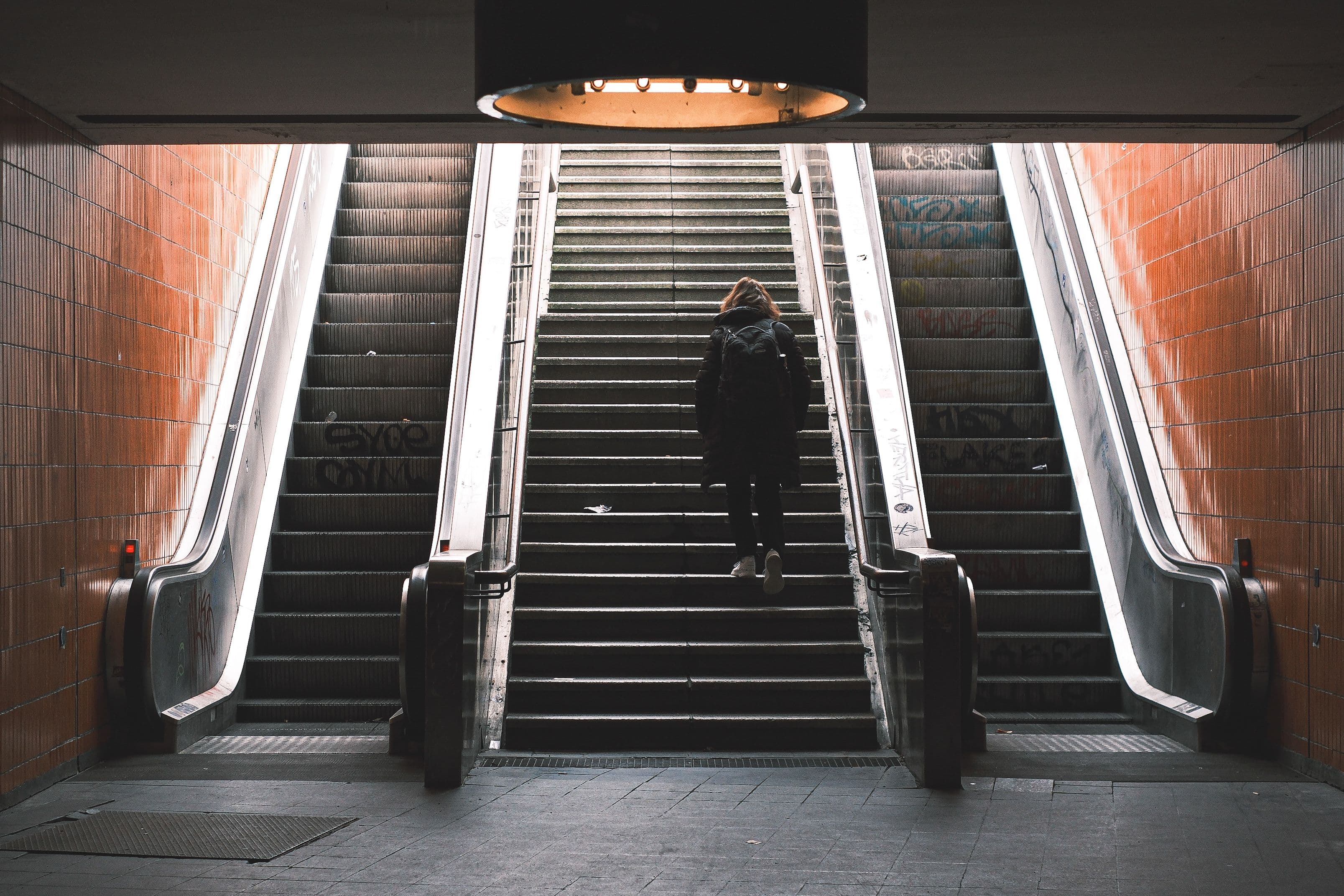 A person taking the stairs beside escalators, representing simple movement choices and habit stacking